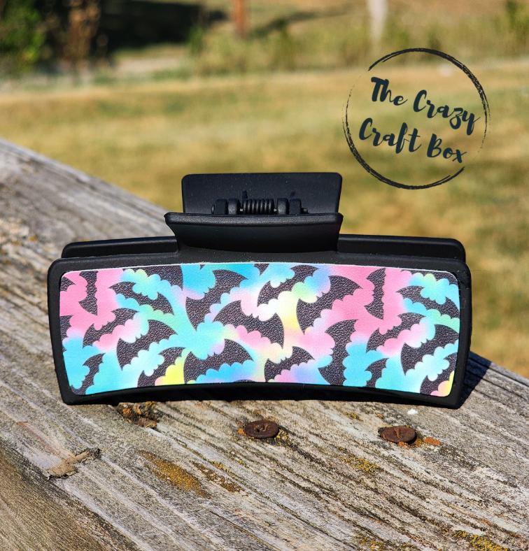 Whiskers n Bows Halloween hair claw clip featuring a black frame and a colorful pastel bat pattern on a wooden fence.