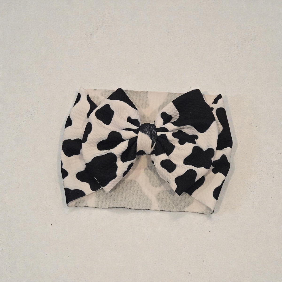 Whiskers n Bows black and white cow print baby headband with a large fabric bow on a textured white background